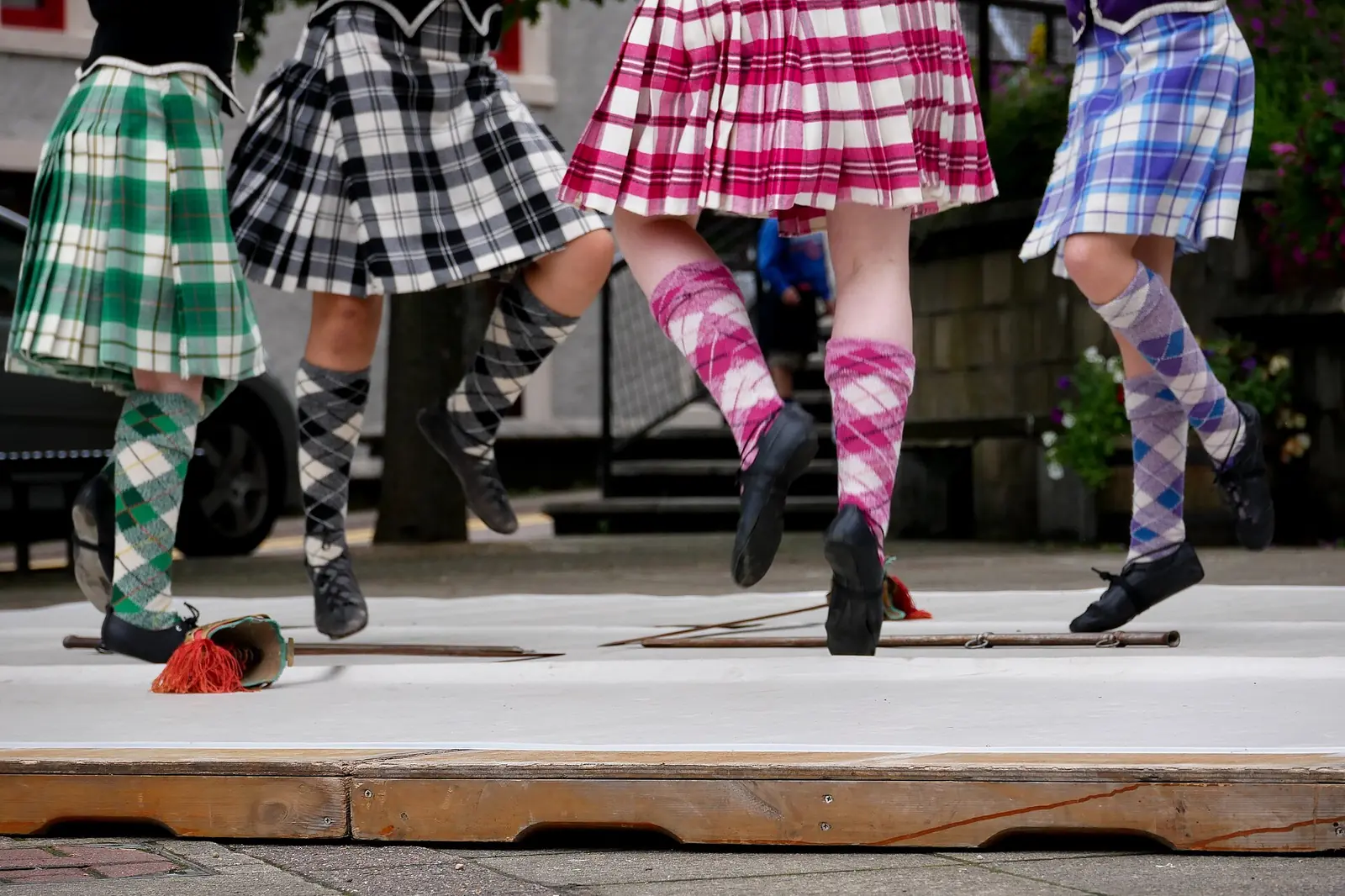Highland dancers in tartan kilts and patterned socks dance beside swords laid on a white board